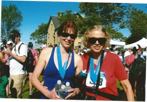 Two women with finisher medals and race bibs at a race event.
