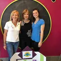 Three women standing together in front of a pink wall with a large circular sign